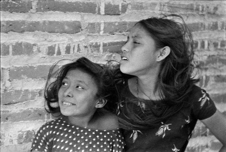 Two young girls in front of a brick wall looking to their right.